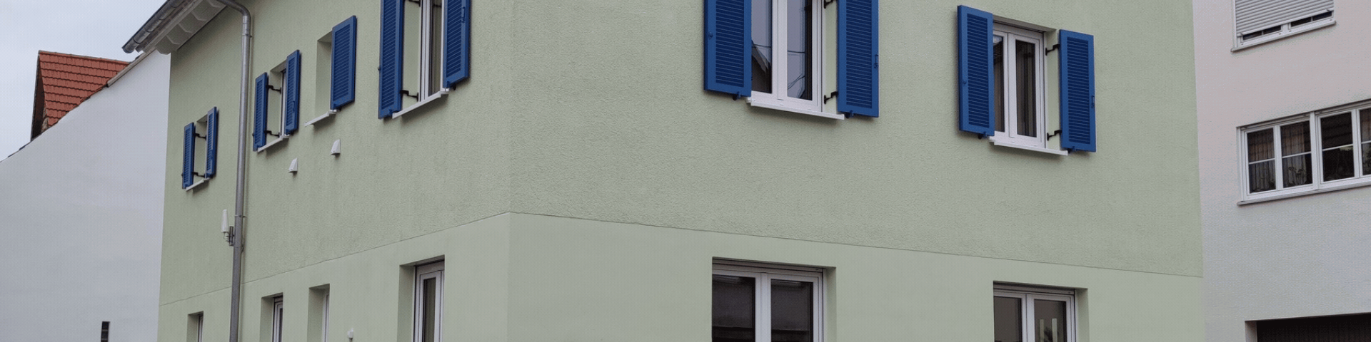 Two-story building with pale green walls and bright blue window shutters, white-framed windows along the facade.